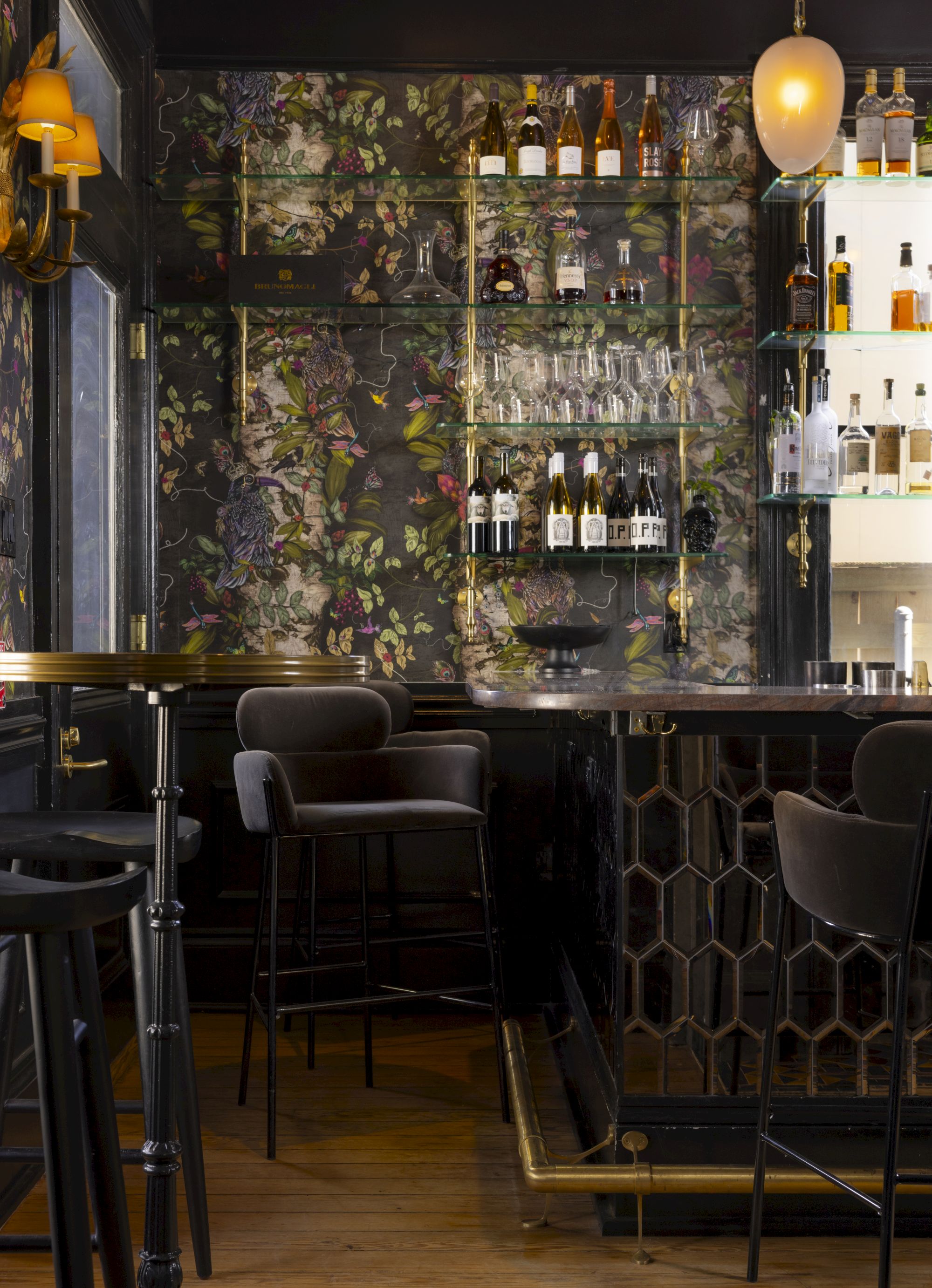 A stylish bar interior with patterned walls, shelves of bottles, high stools, and soft lighting.