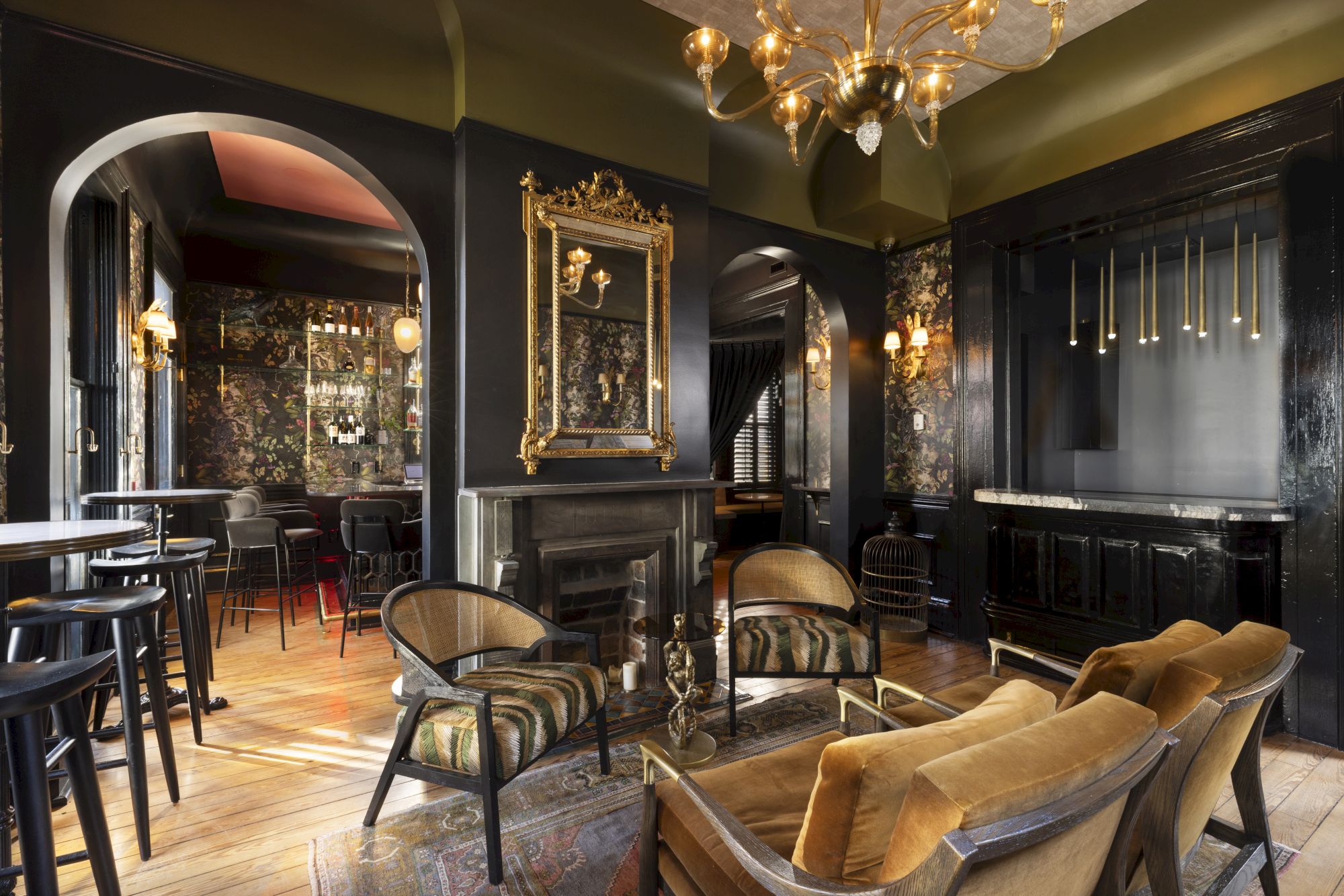 A luxurious room with dark walls, elegant furniture, gold-framed mirror, chandelier, and a mix of modern and classic decor elements.