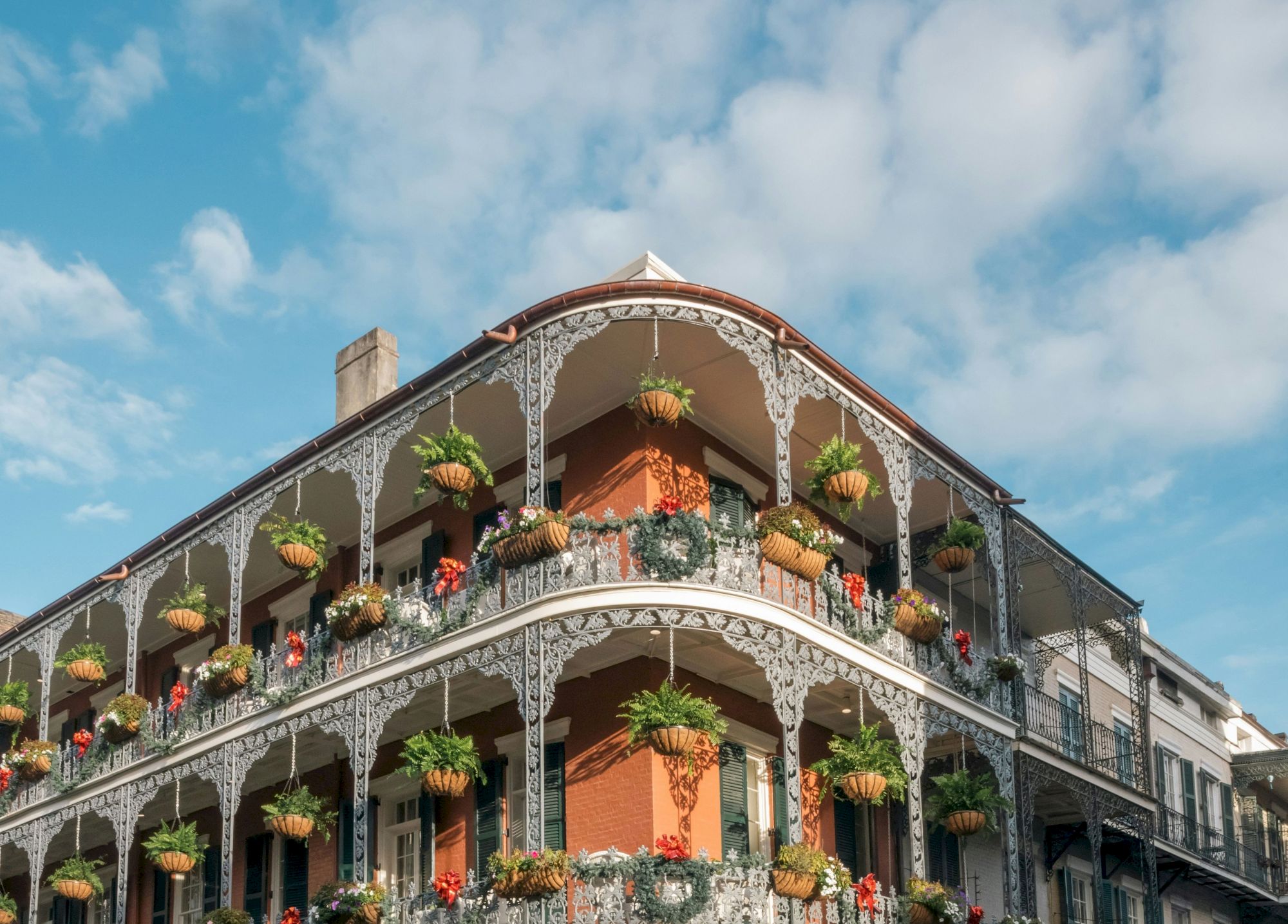 A historic building with ornate ironwork and hanging plants on the balconies under a blue sky with clouds.