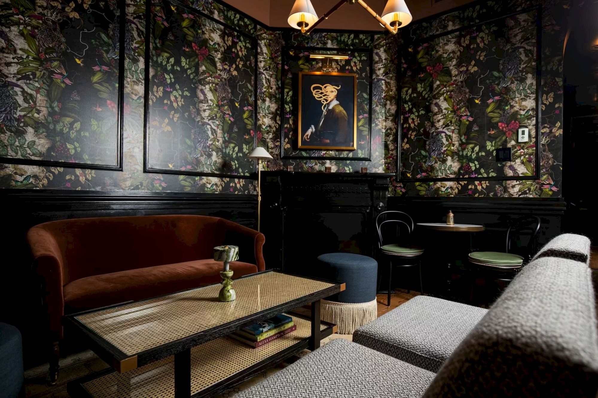 A cozy, stylish room with floral wallpaper, sofas, a table, art, and ambient lighting creates an inviting atmosphere.