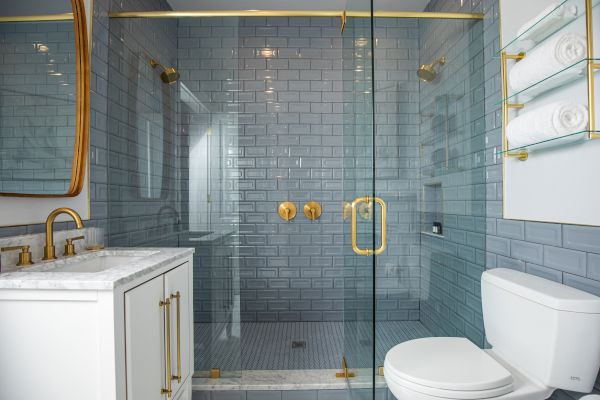 A modern bathroom with a glass shower enclosure, gold fixtures, white cabinetry, and a toilet. Towels are neatly arranged on a rack.