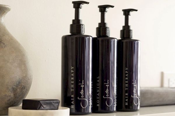 Three dark pump bottles labeled "Hair Therapy" and a small bar on a dish positioned on a shelf.
