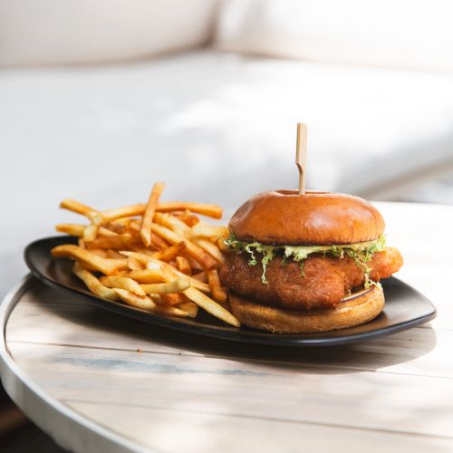 A burger with lettuce and sauce, served on a black plate with a side of French fries on a table.