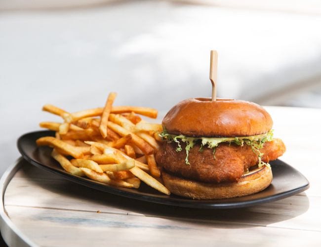 A burger with lettuce and sauce, served on a black plate with a side of French fries on a table.
