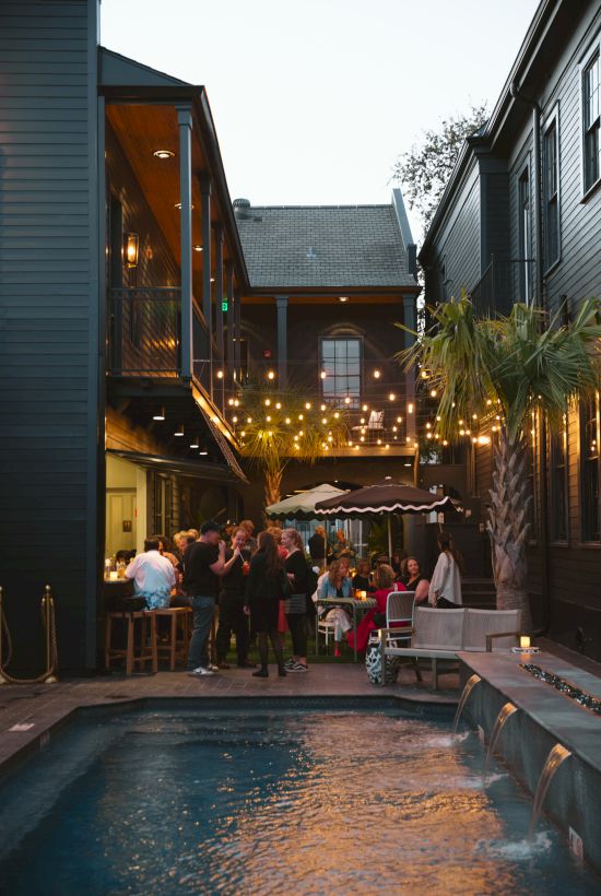 An outdoor gathering near a small pool, with people dining and string lights above in a cozy courtyard setting.