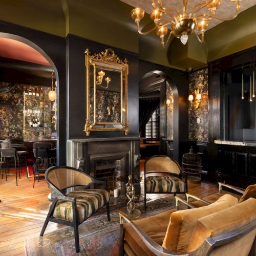A stylish interior with vintage decor, featuring elegant furniture, a fireplace, and ornate lighting, creating a cozy atmosphere.