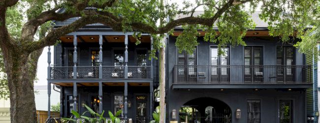 A dark-colored, two-story house with balconies and a large tree in front, providing a cozy and mysterious ambiance.