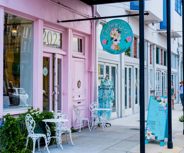 The image shows a charming pink café with ornate chairs and tables outside, featuring a round sign and decorative banner.