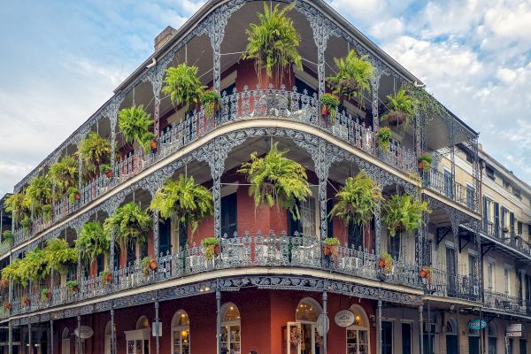 A historic building with ornate iron balconies and hanging plants on a street corner, likely in a Southern U.S. city.