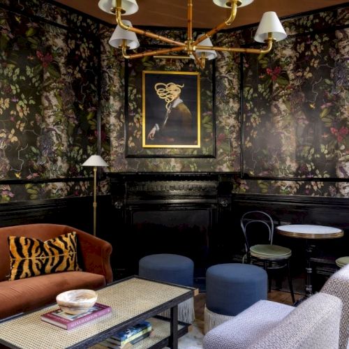 A stylish room with floral wallpaper, vintage lighting, eclectic furniture, and art creates an inviting and cozy atmosphere.