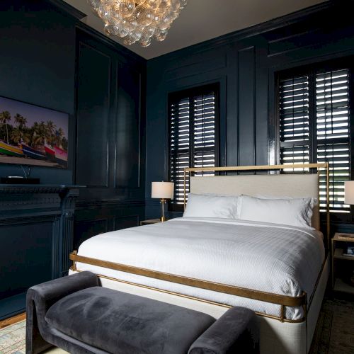 A luxurious bedroom with a white bed, dark walls, chandelier, and TV, creating an elegant and cozy atmosphere.
