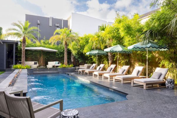 A modern backyard pool with lounge chairs, umbrellas, and lush greenery creates a relaxing outdoor space.