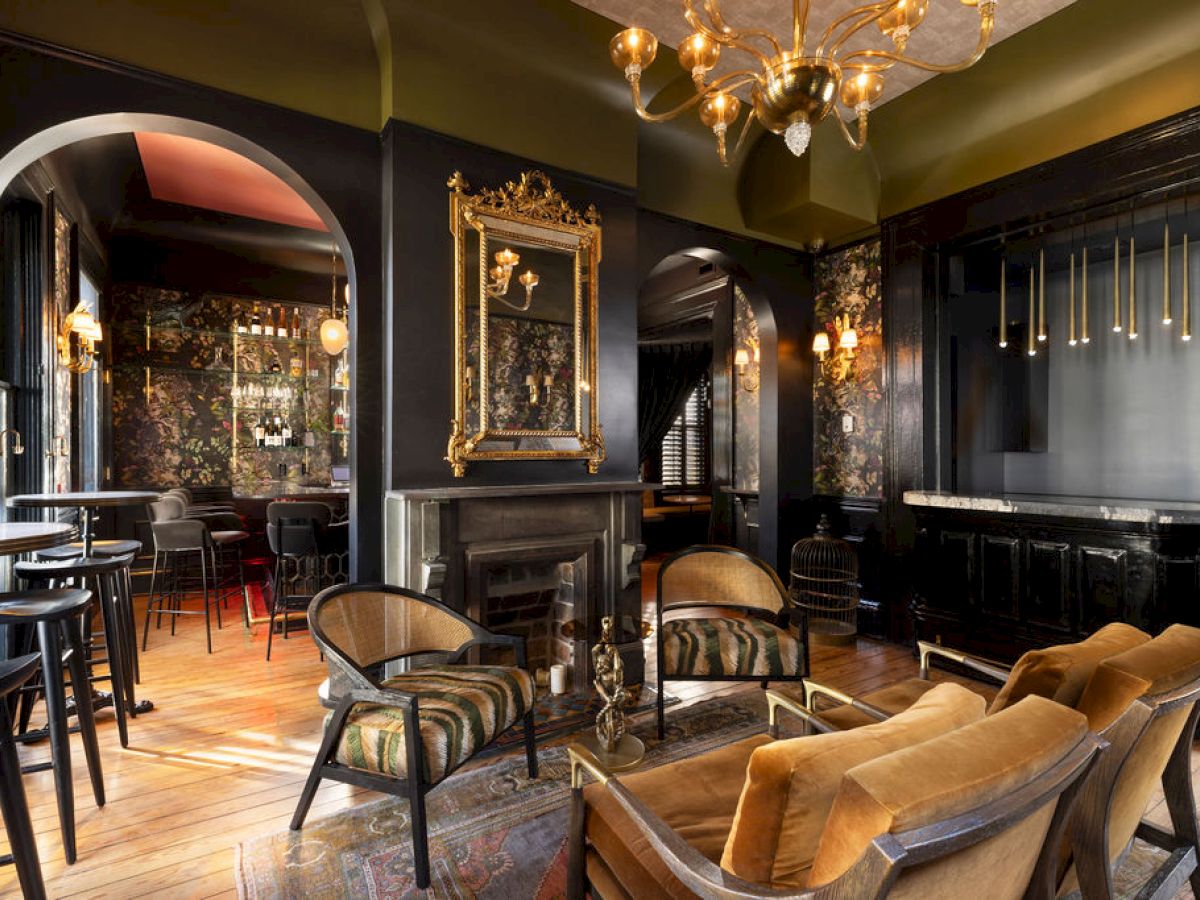 A stylish, cozy interior featuring a vintage fireplace, elegant seating, gold accents, and sophisticated dark tones throughout the space.