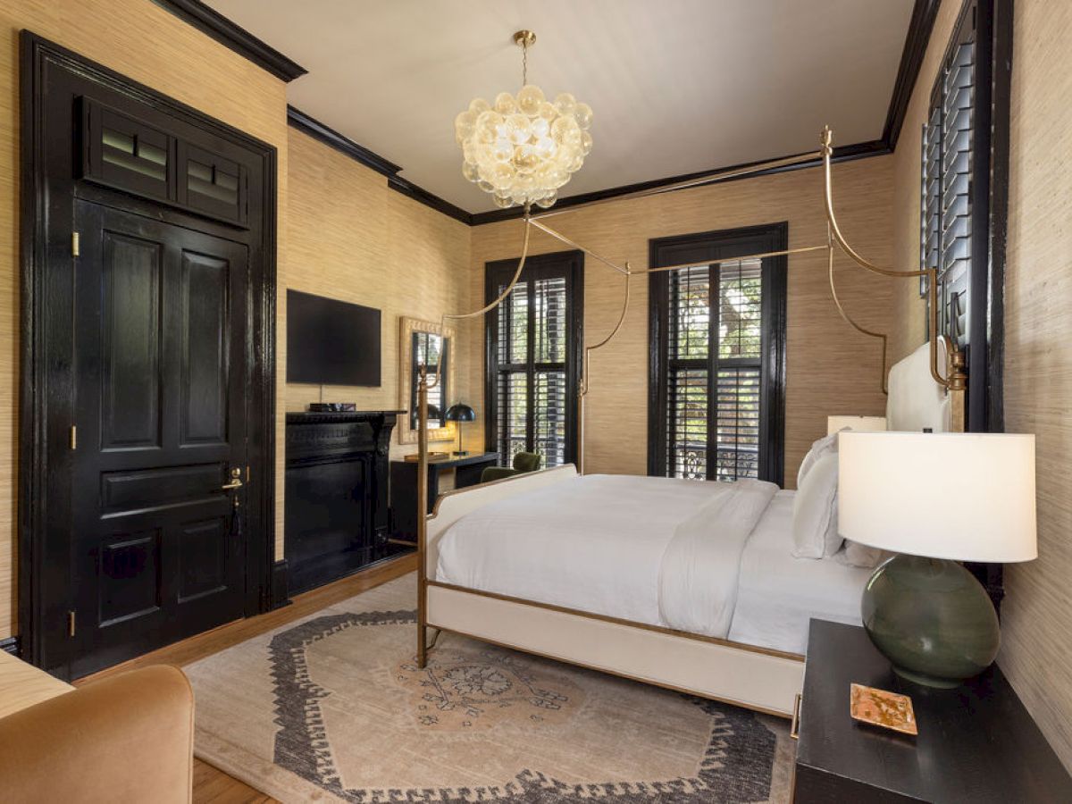 A cozy bedroom with a bed, chandelier, TV, armchair, lamps, and elegant decor in a warm color scheme.
