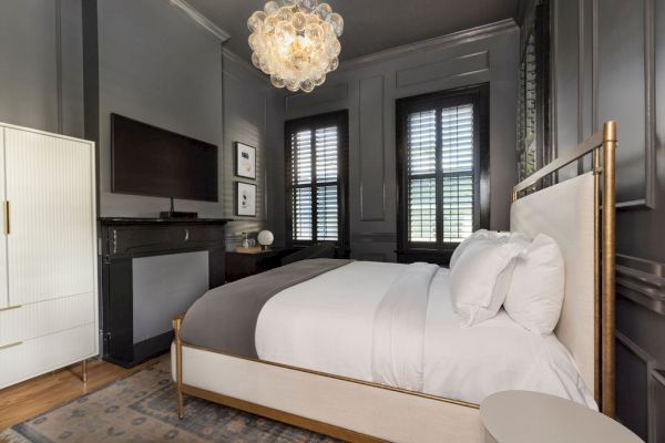 A stylish bedroom with a double bed, modern chandelier, dark walls, large windows, and minimal decor, creating a cozy and elegant atmosphere.
