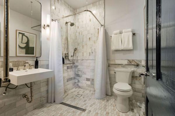 A modern bathroom with a walk-in shower, curtain, wall-mounted sink, toilet, towels, and a framed abstract artwork on the wall.