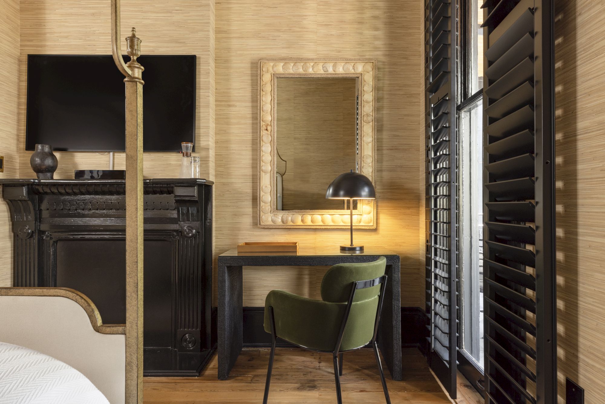The image shows an interior with a desk, green chair, mirror, lamp, TV, and fireplace, alongside tall shutters.