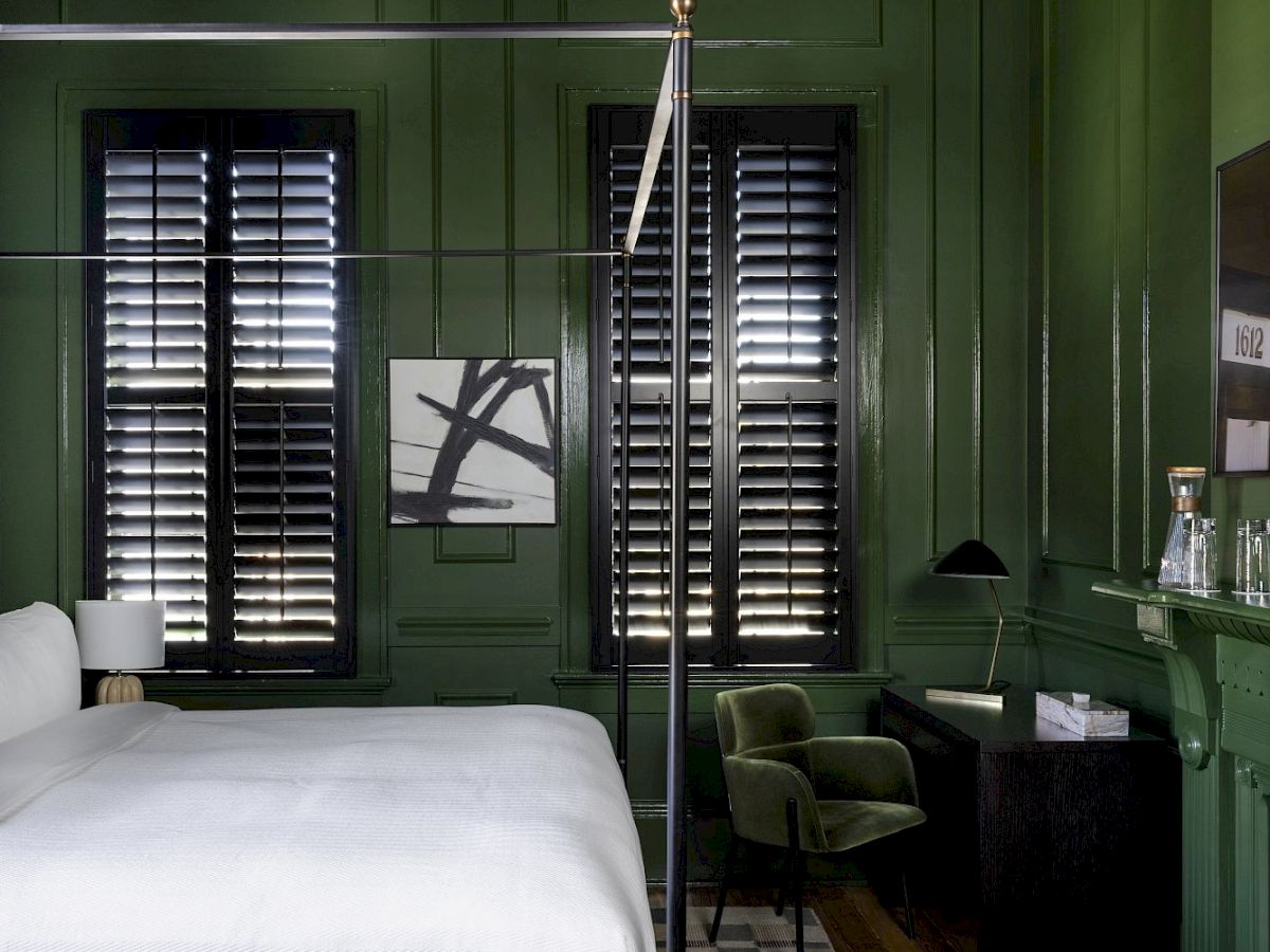 A stylish bedroom with green walls, a four-poster bed, a checkered rug, a chandelier, and modern decor.
