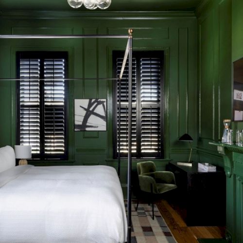A room with a green color theme, featuring a bed, chandelier, shutters, artwork, chair, and rug, creating a stylish interior design.