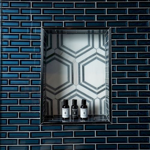 The image shows a recessed shelf with three small bottles against a hexagonal-patterned wall, surrounded by dark blue brick tiles.