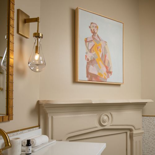 This image shows a bathroom with a framed artwork, shelves with towels, a mirror, a sink, and a light fixture in a warm, neutral palette.