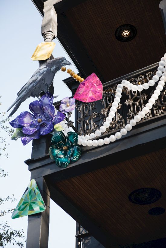 A decorative balcony with a raven, colorful flowers, gems, and beads hanging in a festive arrangement.