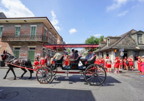 A horse-drawn carriage travels down a street with people dressed in red walking nearby, under a clear blue sky.